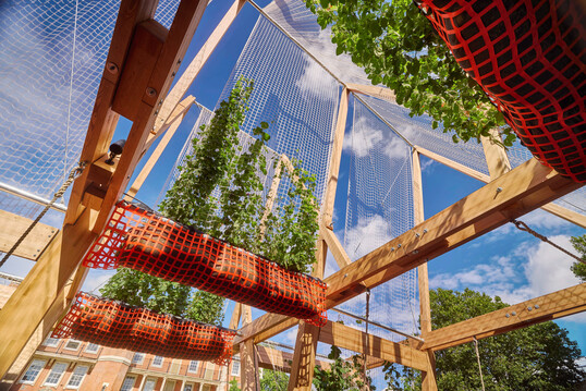 In Zusammenarbeit mit dem American Hardwood Export Council entstand f�r das London Design Festival 2024 das publikumswirksame Vert | Triangel mit schwingenden Sitzb�nken unter Laubd�chern.