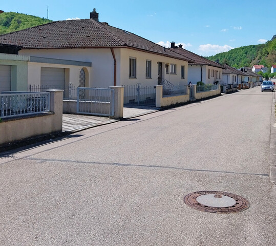 Siedlungsstraße ohne Grün, bei der sogar die Privatgrundstücke versiegelt sind. Hier spürt man förmlich die glühende Hitze im Sommer.