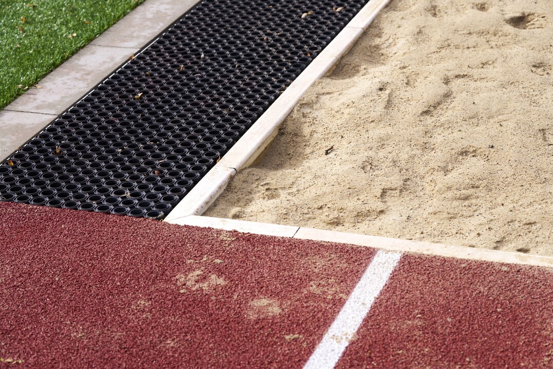 Elastic-Randsteine umfassen die Sprunggrube und Sandfangrinnen halten ausgetretenen Sand von dem angrenzenden Belag fern.