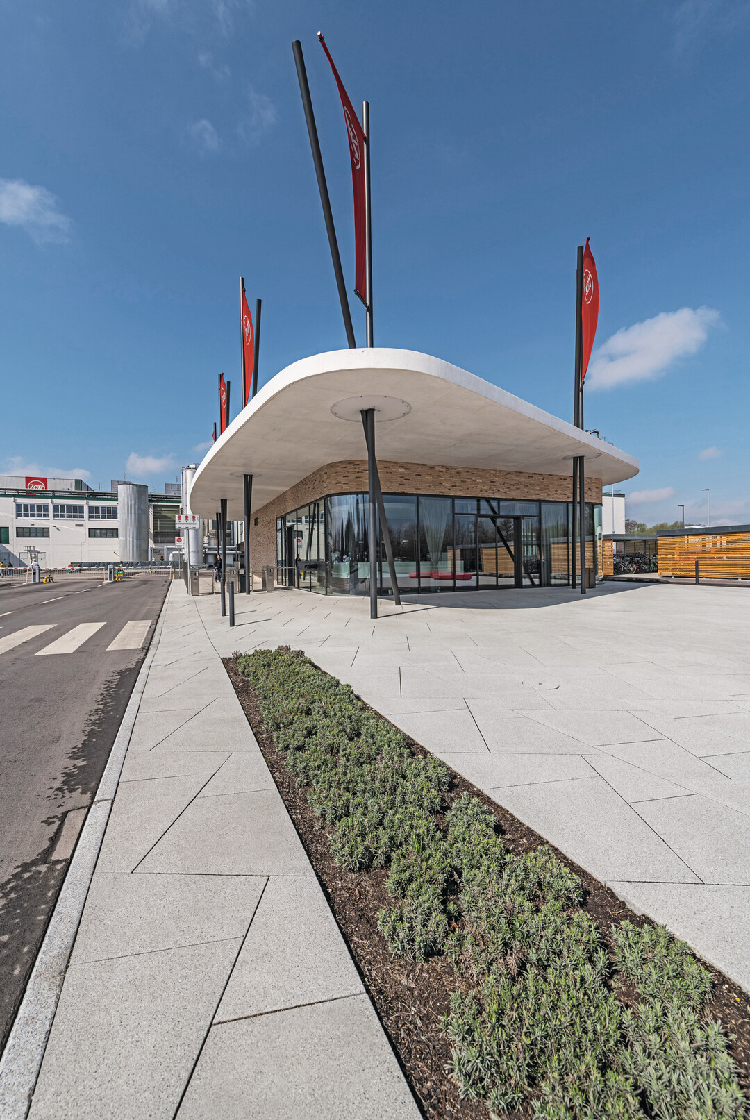 Zugang zu Zott. Die Fassade spiegelt die zickzackförmige rote Bank wider, die das Firmenlogo stilisiert.